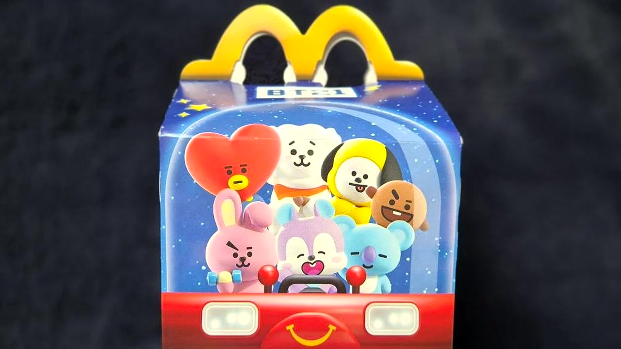 BT21 Happy Meal kutija s likovima KOYA, RJ, CHIMMY, SHOOKY, COOKY, MANG i TATA na tamnoj podlozi.